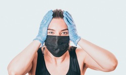 studio shot on white background of a sick young woman wearing mask and latex gloves, stressed by quarantine.