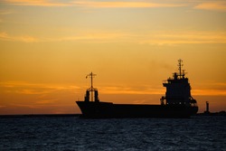 a silhouette of a cargo ship at sunset.