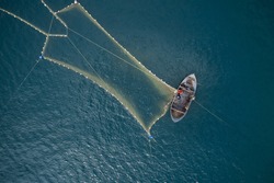 Vintage wooden boat in coral sea. Boat drone photo. A fisherman on a fishing boat is casting a net for catching fish.