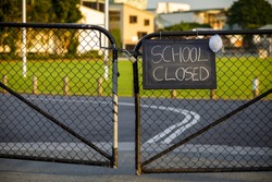 school closed sign with protective mask hanging on a padlocked gate, school closed or shutdown concept amid coronavirus fears and panic over contagious virus spread of the pandemic outbreak