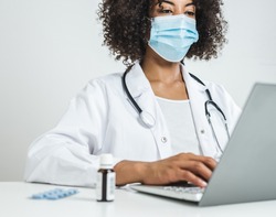 afro female doctor with surgical mask in her office using a laptop