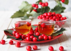 The hawthorn harvesting season for future use. Alternative medicine. The benefits of herbal hawthorn tea. Two cups of herbal tea on a red rectangular plate on a white table with berries.
