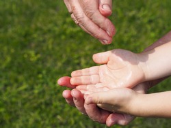 The concept of heritage and nature conservation on Earth.Water pours into the hands of a child in the hands of an older grandmother against a background of green grass.