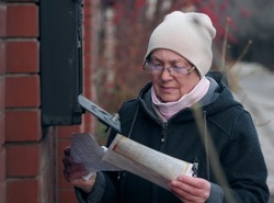 An elderly woman opened a mailbox on a fence on the street with a key and reads the correspondence she received. A moment in the life of a pensioner.