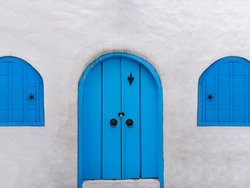 White wall with an arch old light blue traditional door and windows made from woods. Santorini architecture style.