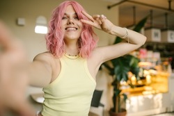 A cute girl with pink hair poses for the camera, laughs and makes faces. A bright girl takes a selfie in a cafe.