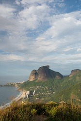 Early morning light over Pedra da Gavea and Sao Conrado Beach from Morro Dois Irmaos - Two Brothers Hill in Rio de Janeiro. There are clouds and blue sky with light on the tall rock mountain face.