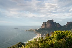 Early morning light over Pedra da Gavea and Sao Conrado Beach from Morro Dois Irmaos - Two Brothers Hill in Rio de Janeiro. There are clouds and blue sky with light on the tall rock mountain face.
