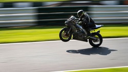 A panning shot of a grey racing bike on one wheel as it circuits a track