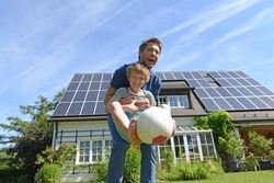 Father and son playing with ball in garden of solar paneled house