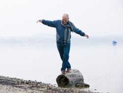 A senior man balancing on a log at the edge of a lake