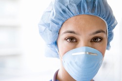 Young female nurse at camera wearing surgical mask and scrubs