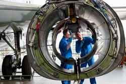 Engineers in uniforms inspecting the engine casing of a passenger jet at a hangar.