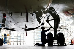 Wide shot of an engineer inspecting the landing gear of a passenger jet at a hangar.