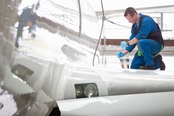 Wide shot of an engineer repairing the wing of a passenger jet at a hangar.
