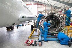 Wide shot of engineers assembling an engine of a passenger jet at a hangar.