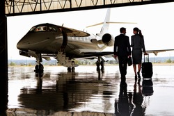 Wide shot of a businesswoman and a businessman walking towards private jet