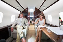 Close up of a smiling couple making a toast with champagne glasses in a private jet