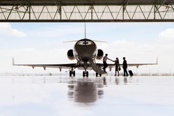 Silhouette of pilot greeting businessman and businesswoman boarding private jet in hangar