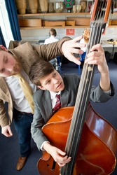 High angle shot of a middle school student playing a double bass in a music class with a music teacher guiding him.