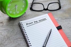 A notebook with Brown Bag Session message. A pen, eyeglasses, and alarm clock at the side.