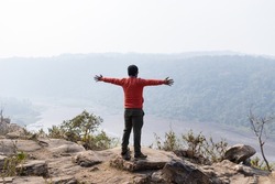 A man with outstretched hands standing on hill top facing backside and enjoying nature
