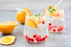 Hard seltzer cocktail with orange, cranberry and mint in glasses and cut oranges on the table. Alcoholic beverage