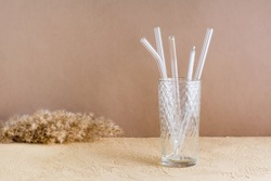 Glass reusable straws for drinks and cleaning brush in a glass on a beige textured background. Sustainable lifestyle.