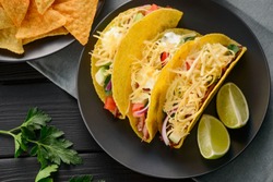 Hard-shell tacos and nachos, flat lay. Tortillas filled with cheese, vegetables and meat, and served with lime slices.