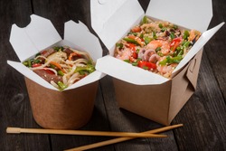 Japanese takeaway food packaged in special boxes. Chopsticks and portions of noodles with chicken meat and rice stirred with vegetables, seafood and soy sauce, then fried in wok.