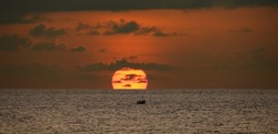 Small fishing boat and the sunset, a small fishing boat sails as the Sun is going down behind the horizon. Scenic seascape photograph.