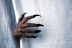 Halloween theme. Zombie hand with black nails on the background of a white sheet. Place for text. Side view.