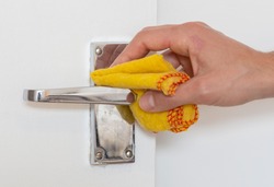 Man cleaning a door knob. Cleaning a silver handle with a yellow chiffon. Disinfecting to kill germs, viruses and bacteria