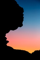 Silhouette of isolated cliff on gradient rose blue sky background 