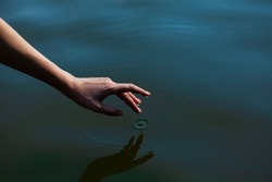 a woman's hand gently touches the water in the pond, a close horizontal photo on the theme of tranquility