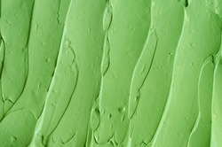 Green cosmetic clay (cucumber facial mask, avocado face cream, green tea body wrap) texture close up, selective focus. Abstract background with brush strokes