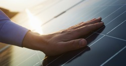 Close up of an young engineer hand is checking an operation of sun and cleanliness of photovoltaic solar panels on a sunset. Concept:renewable energy, technology,electricity,service, green,future