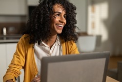 Cinematic shot of young brazilian business woman is controlling email on laptop while working in kitchen from home, exulting and celebrating successful deal or promotion in her career.