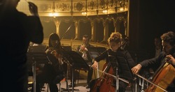 Cinematic Shot of Symphony Orchestra Musicians Performing on the Stage of a Classic Theatre During a Classical Music Concert. Focused Performers Playing Different Instruments