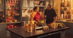 Indian Couple Exploring Traditional Cooking: Preserving Culinary Heritage, Preparing Authentic Recipes with Love and Care. Laughing and Having Fun in the Kitchen, Bright Sunny Festive Day. Medium Shot