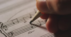 Macro close up of musician or composer hand writes a song or a musical work, writing notes with pencil on the pentagram. Concept: conservatory, music, composer, notes, art, life