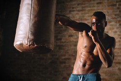 An African American guy trains in a vintage gym and fists his boxing bag fists. Concept of: gym, fitness, boxing, success, workout and power