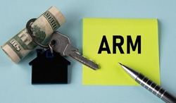ARM (Adjustable Rate Mortgage) - acronym on a yellow sheet of paper on a light background with a house keychain, banknotes and a pen. Business concept