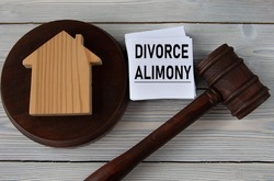 DIVORCE ALIMONY - words on a white sheet against the background of a judge's hammer and a wooden house