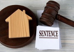 SENTENCE - word on a white sheet against the background of a judge's hammer and a wooden house