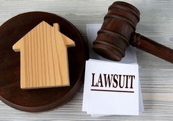 LAWSUIT - word on a white sheet against the background of a judge's hammer and a wooden house