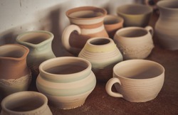 Many clay pot is on the table in pottery. Bright pottery. Many white, not painted clay pottery standing on wooden table. Creative studio potter. Workplace wizard Crock pottery