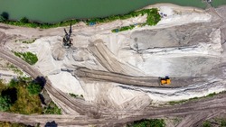 Aerial drone view flight over sand mining. Sand quarry. Top view. Lake with blue water near sand pit. Bulldozer machine moving sand in quarry. Mining industry. Mining equipment at quarry.