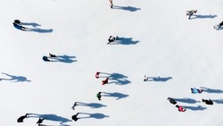 Many people are skating on a white outdoor ice rink in the city on a sunny winter day. Shadows of people skating on the surface of a white ice rink. Aerial drone view. Top view. Lifestyle, sport, rest