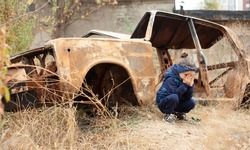 A little girl is crying near the burnt car. War in Donetsk. War Nagorno-Karabakh. Burned-out car.